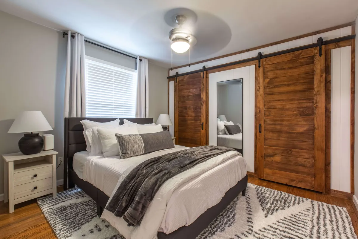 A serene bedroom with a comfortable bed, soft rug, and wooden sliding doors. The gentle lighting and inviting textures create a cozy, restful environment ideal for relaxation and unwinding after a busy day.
