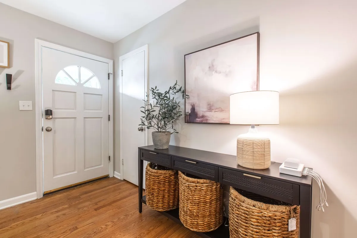 An inviting entryway with the front door in view, a console table, a lamp, stylish baskets, and wall art. The decor creates a warm first impression, smoothly guiding guests from the entrance into the heart of the home.