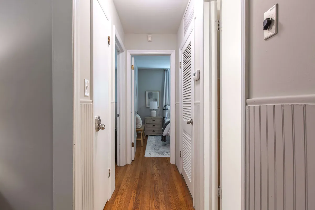 A long hallway with softly lit wooden floors and closed doors leading to different rooms of the house. The inviting ambiance suggests easy access to various practical spaces, such as storage closets or utility rooms, all within a peaceful home environment.