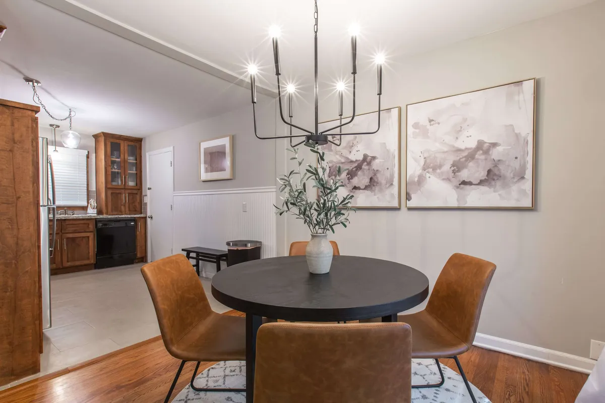 This image features a stylish dining area with a round black table, elegant chandelier, leather chairs, and abstract wall art. The setup is warm and welcoming, ideal for sharing family meals or planning the day's local outings.